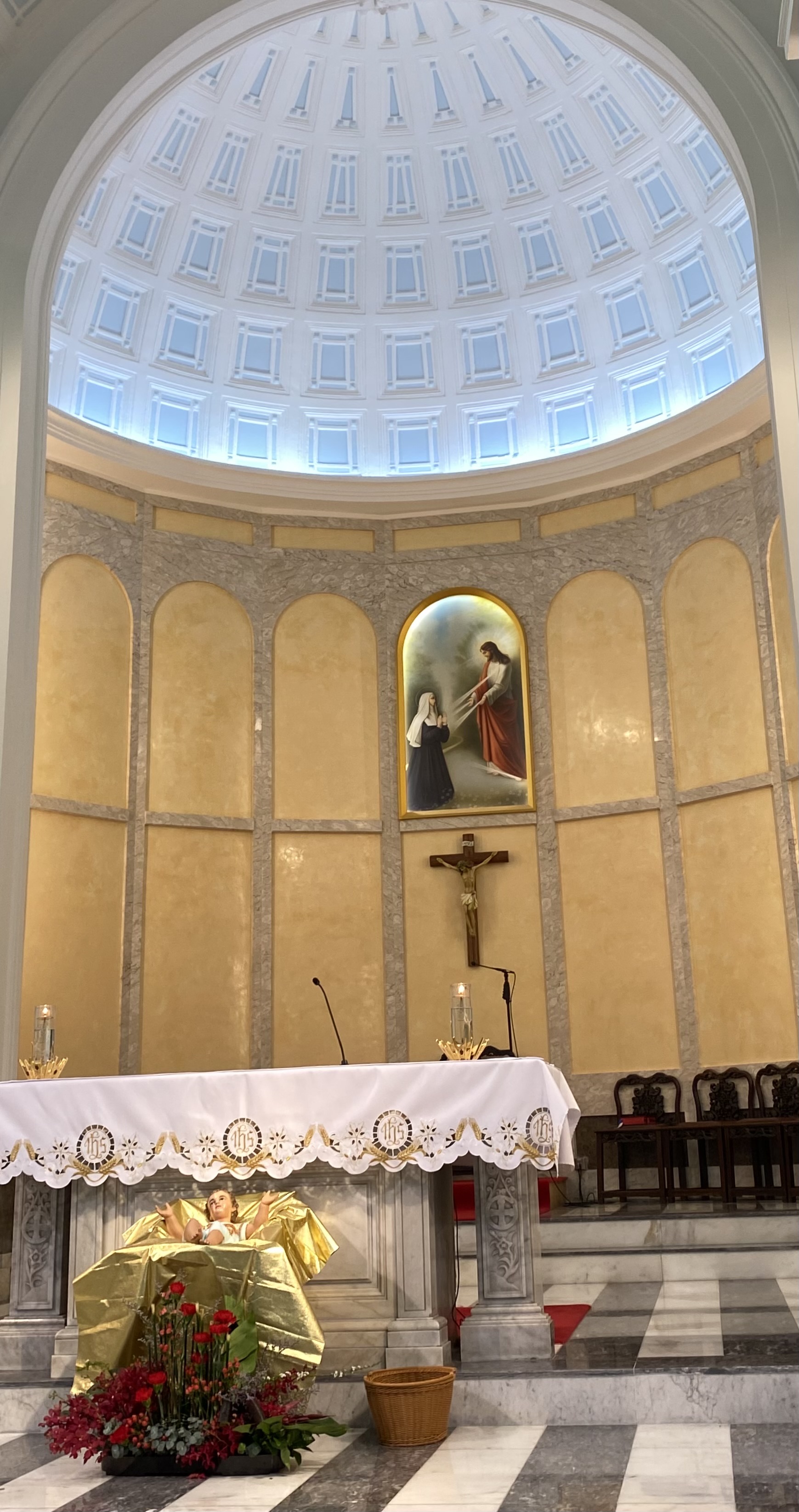 An church altar under a marble arch, on floors of gray and white stripes of marble.  Baby jesus on a gold covered sheet.