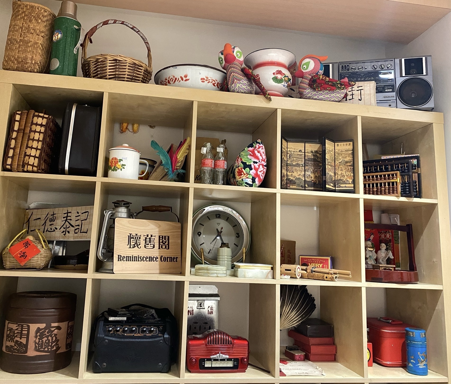 a bookshelf full of Hong Kong retro toys and houseware, e.g. abacuses, enameled hotware bottle and bowl and mug, classic coke bottles, radios, etc.