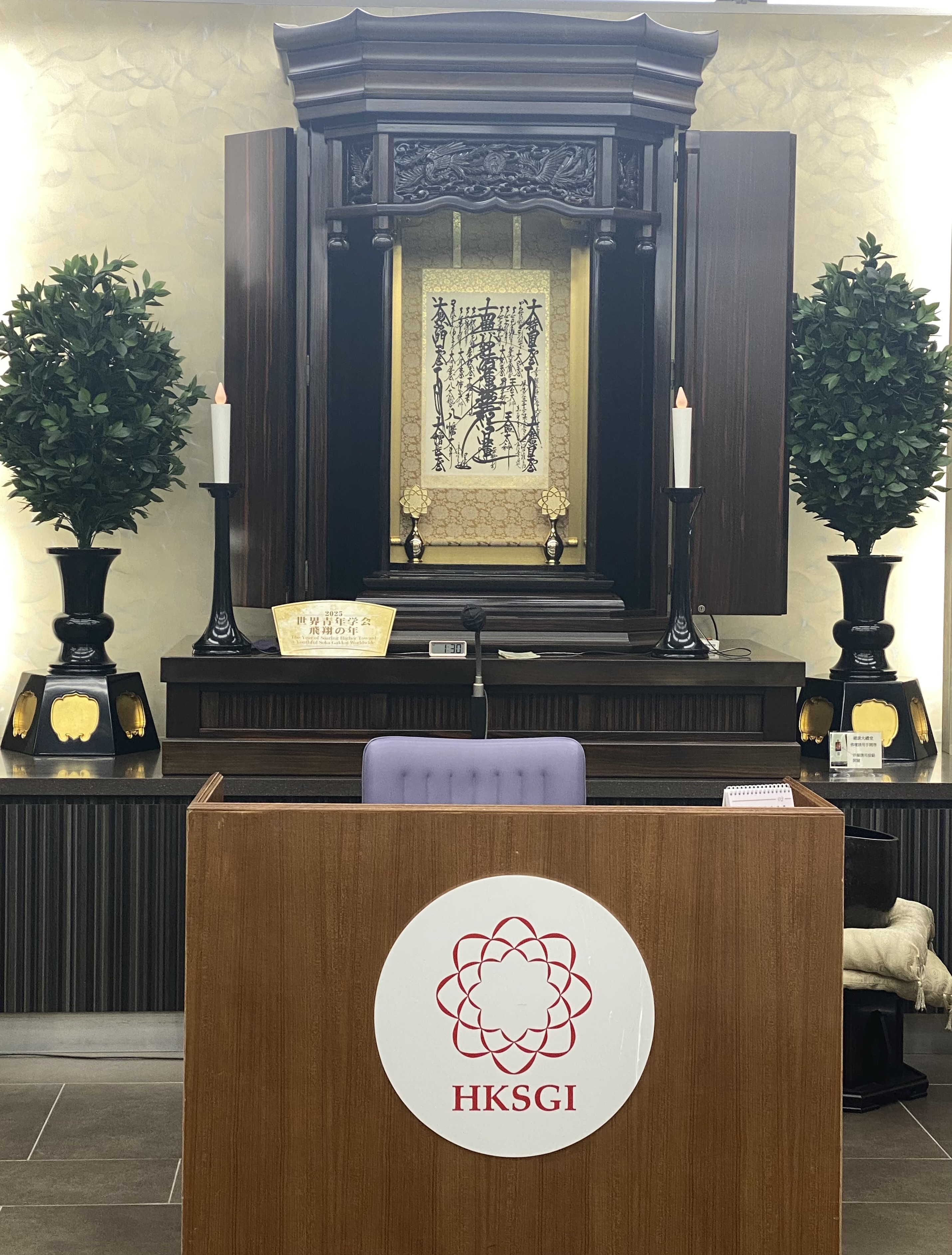 An altar build around a sheet of Chinese calligraphy.  A lectern with a flower logo labeled HKSGI in front.