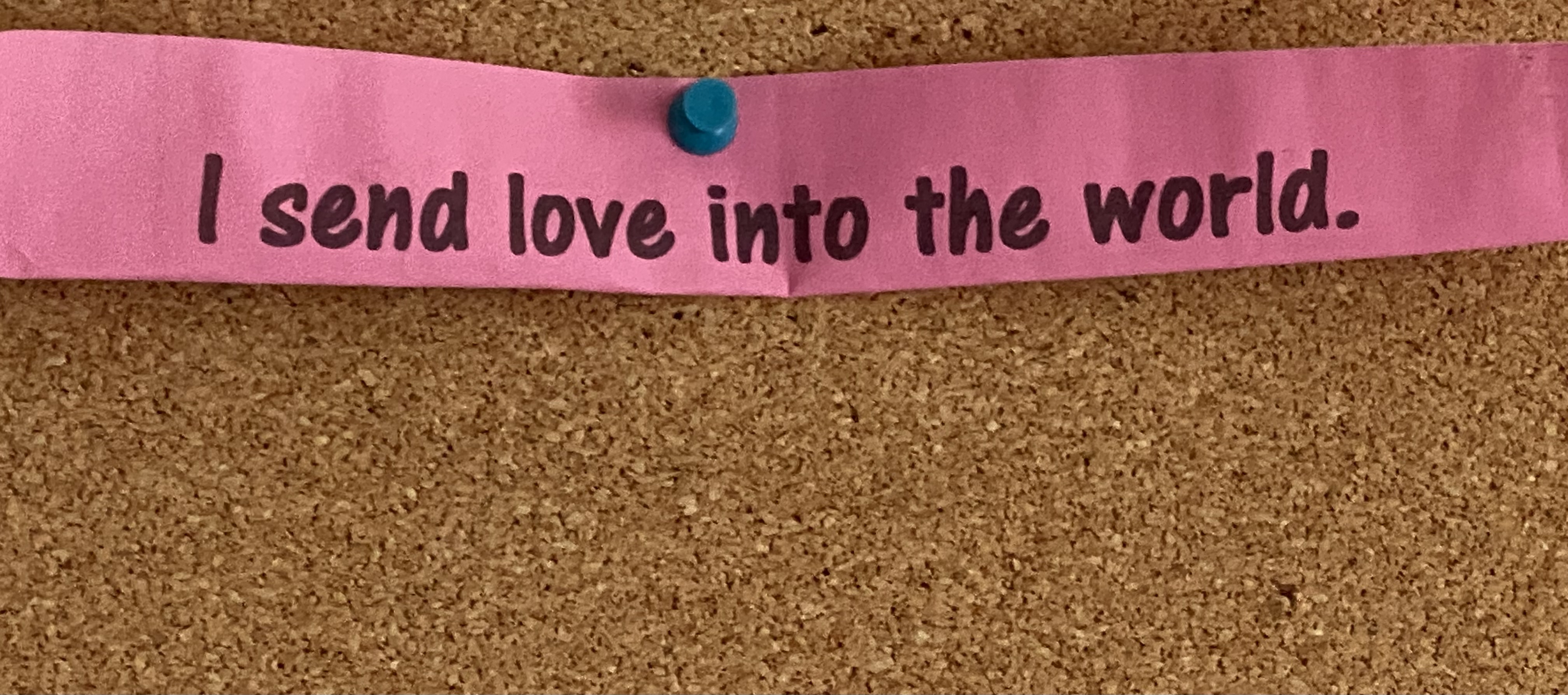 "I send love into the world" printed on a magenta piece of paper, pinned to cork.