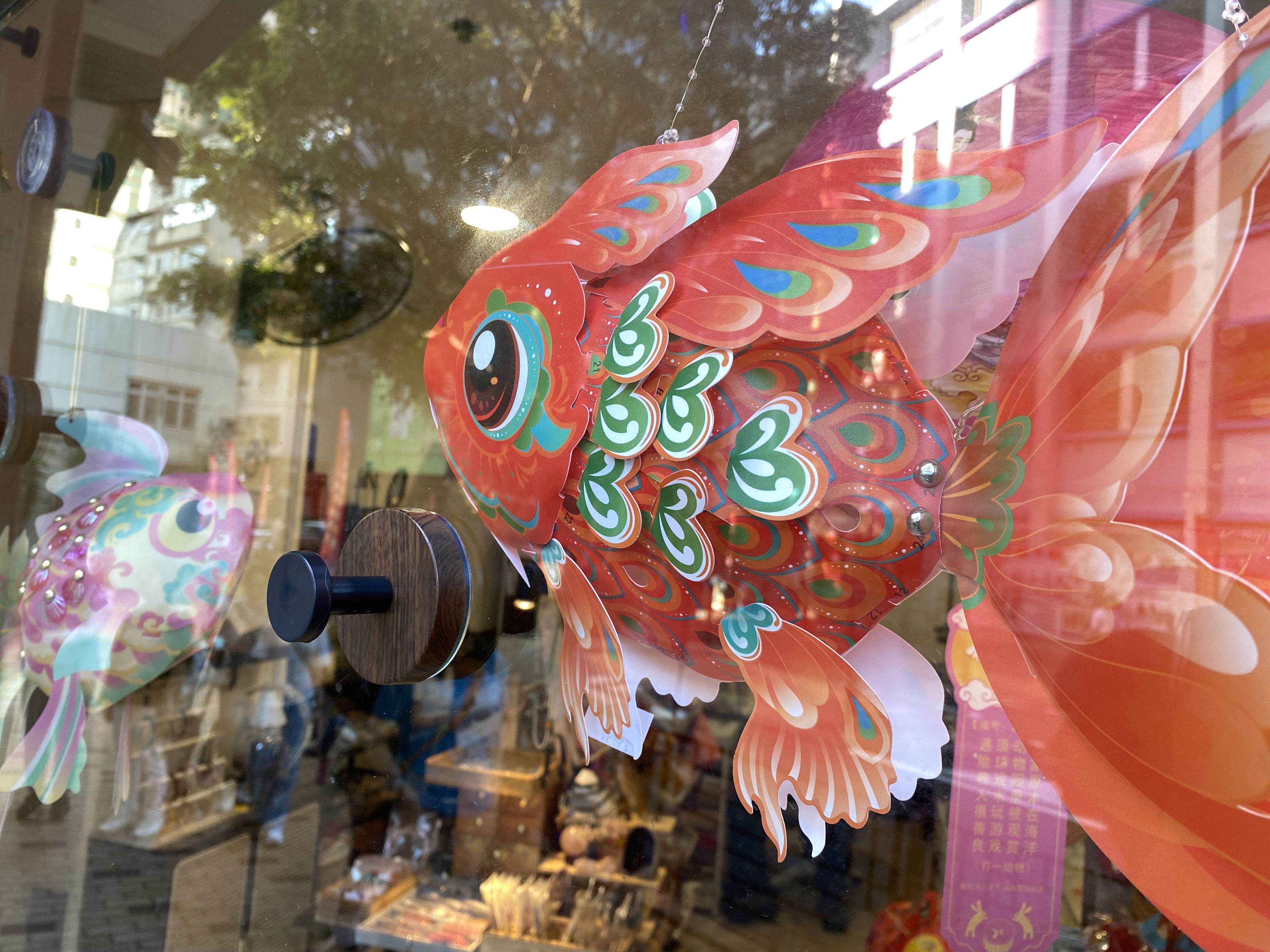 two ornate, colorful lanterns in a store: a red goldfish and a pink goldfish