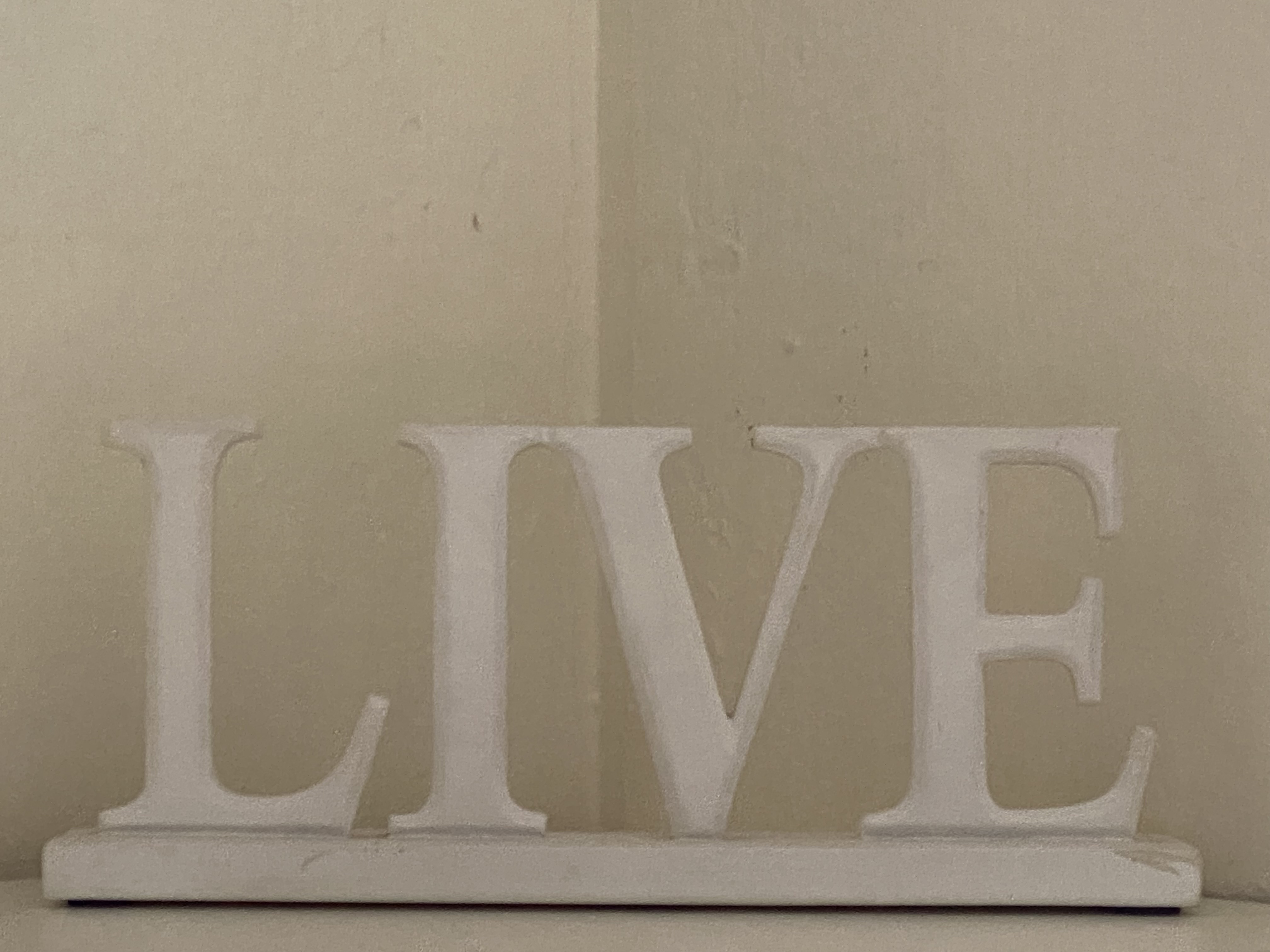 The word "LIVE," white wooden decoration in the corner of a white wall.