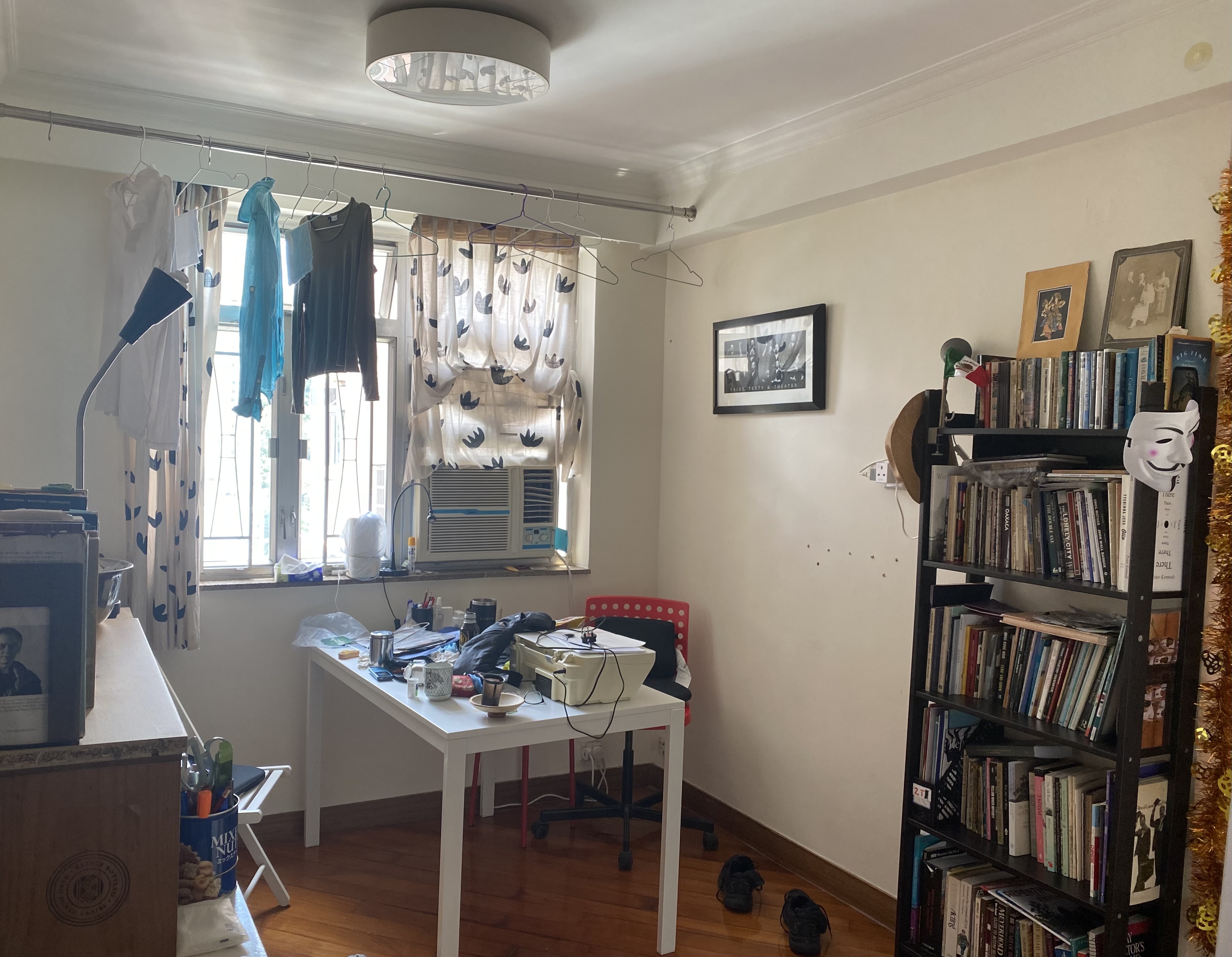 room with side table, dining table, bookcase, air-conditioner and clothes hanging in front of windows