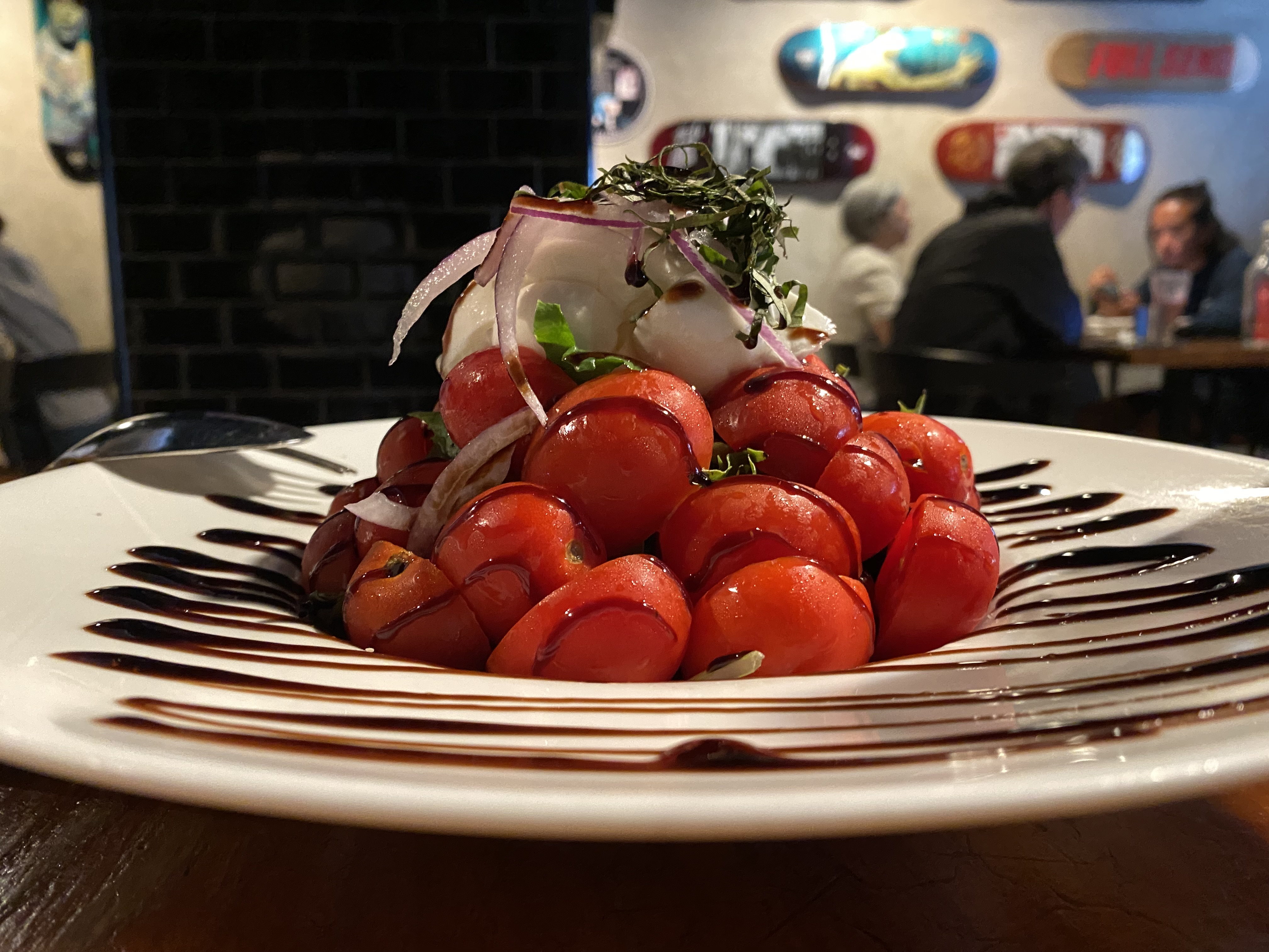 A pyramid of tomatoes with vinegar drizzed in a zigzag pattern.  Diners in the background and art on the walls.