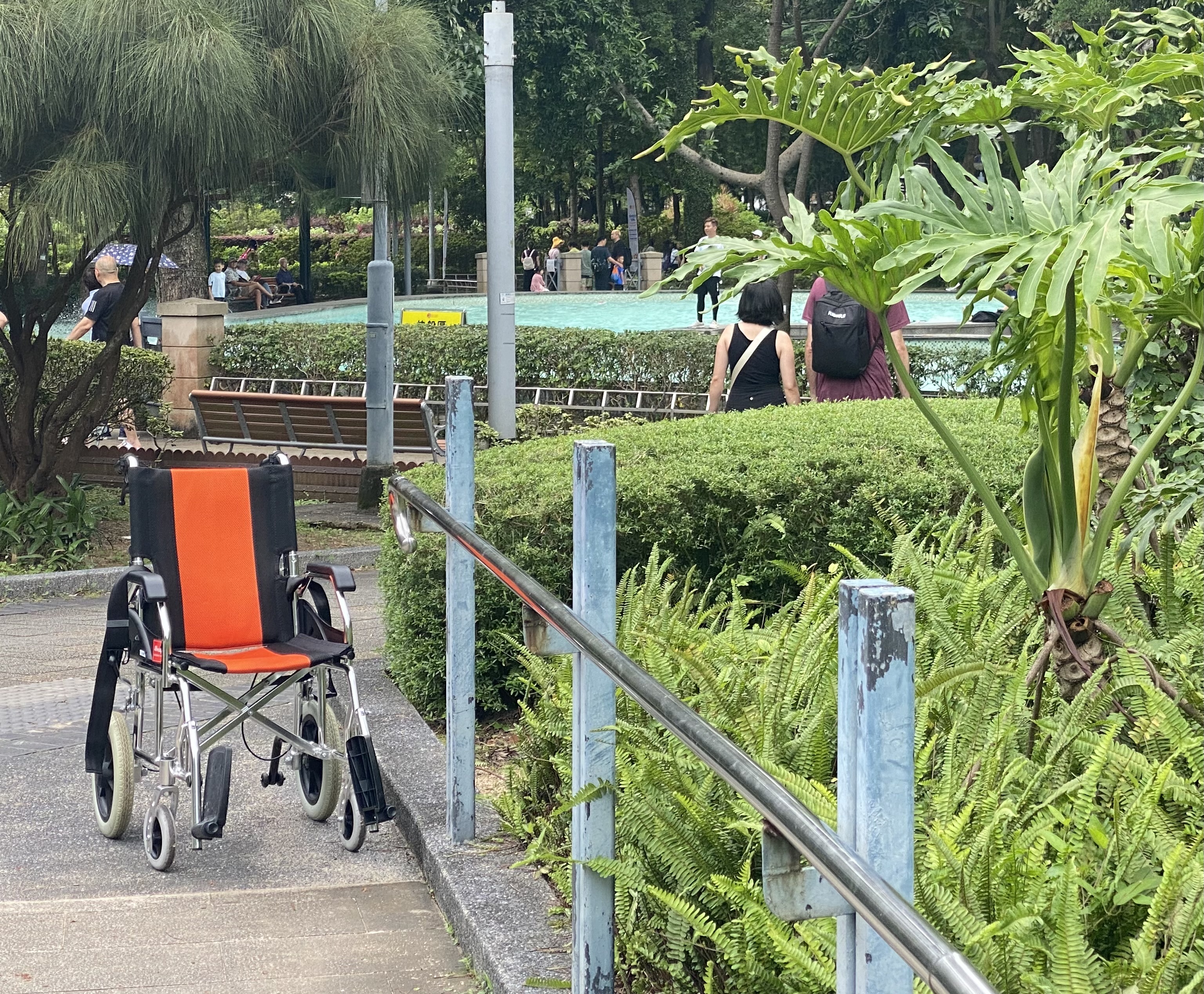 orange and black wheelchair at the end of walkway with metal railing in a park